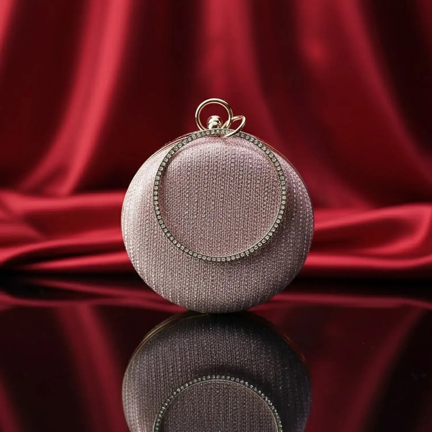 The Manay round rhinestone evening clutch bag on glossy surface with red silk background