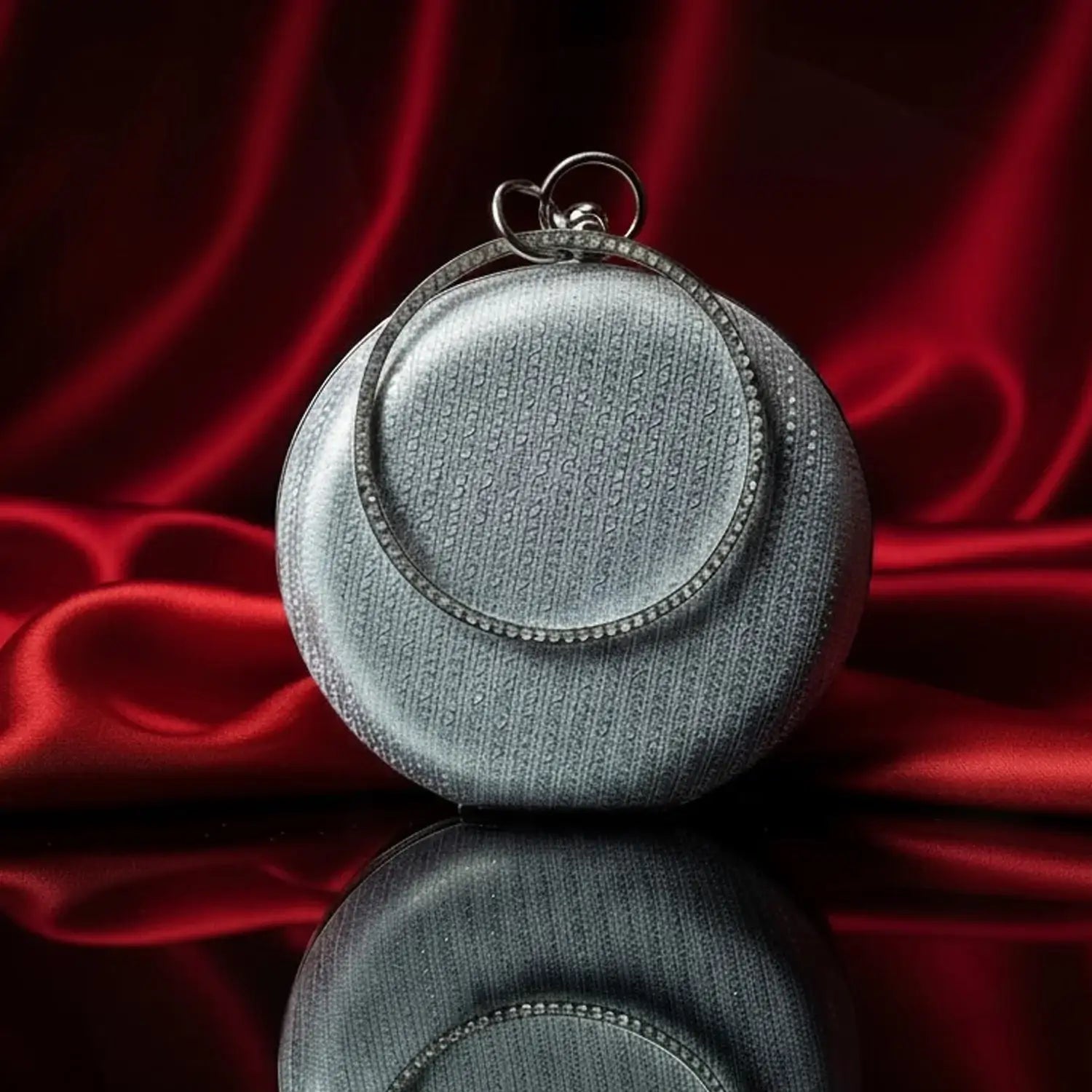 Silver round clutch bag on red silk background, luxury accessory from The Manay
