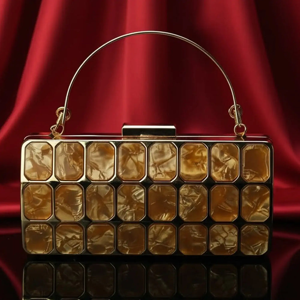 Gold geometric clutch purse on red satin backdrop, luxury fashion bag at The Manay