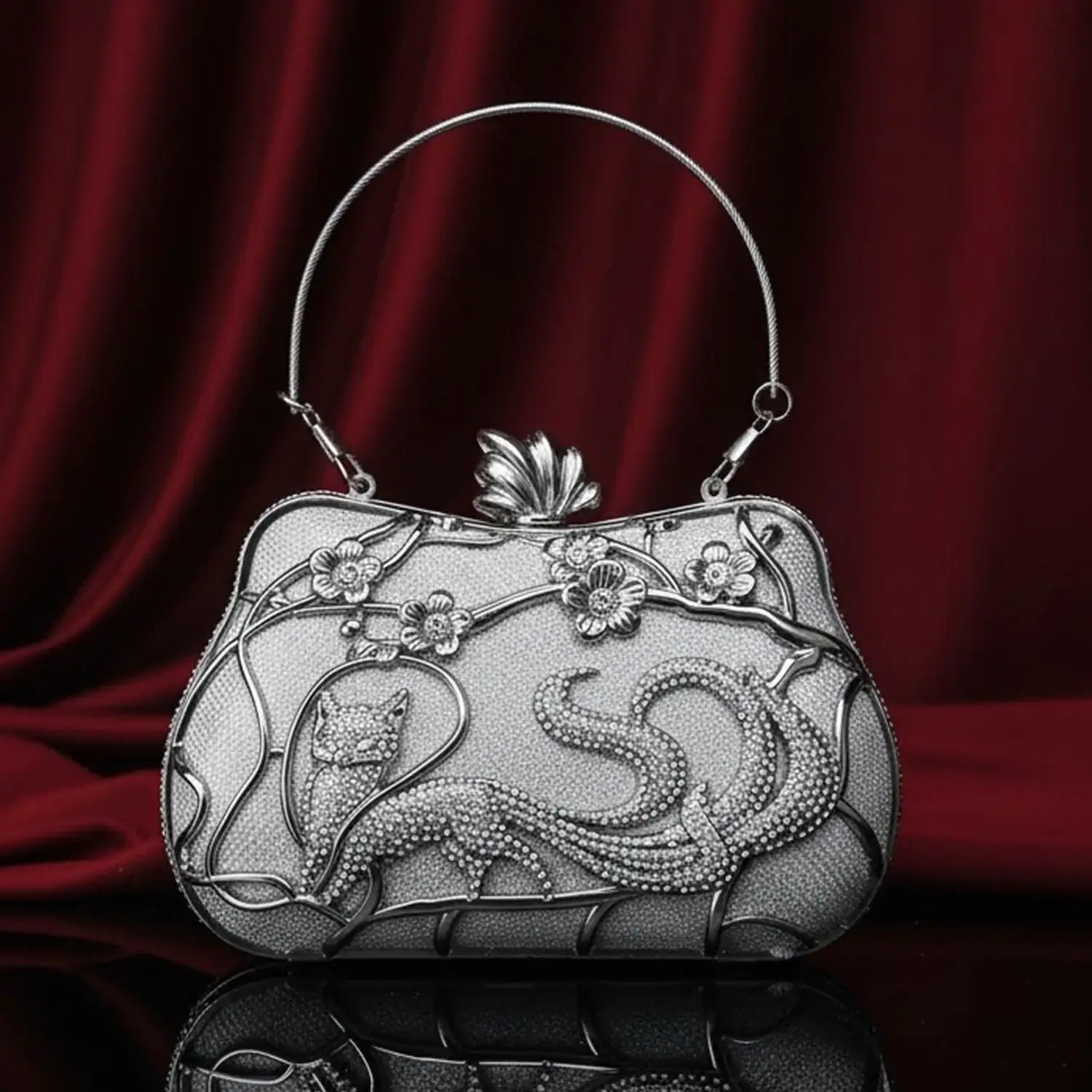 The Manay elegant silver cat evening clutch with floral accents on a red velvet background