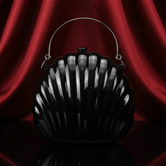 Black shell-shaped handbag with silver handle on red satin background, The Manay fashion