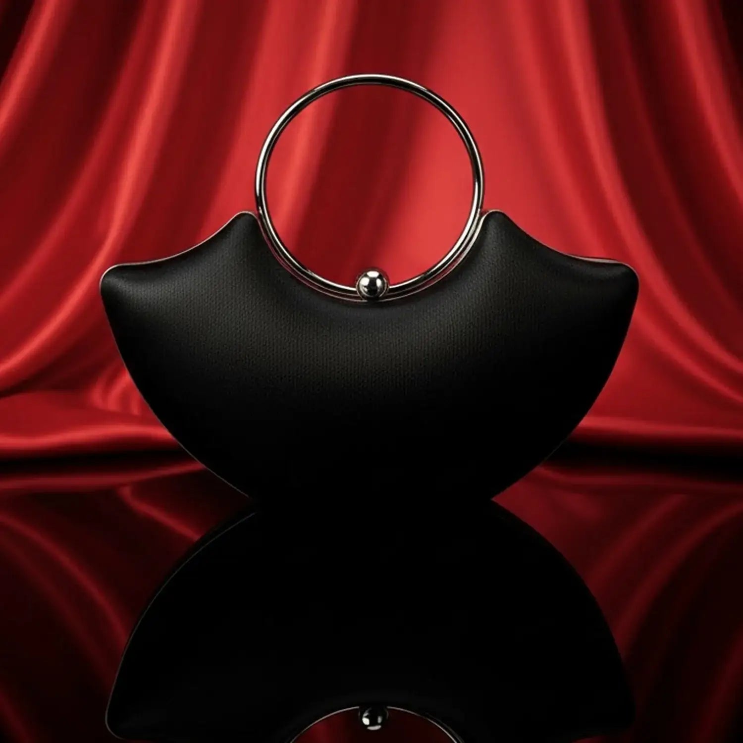 The Manay black designer handbag with silver ring handle on red satin background